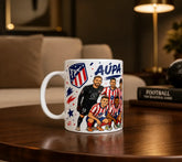 Taza blanca de cerámica con ilustración de los principales jugadores del Atlético de Madrid y el escudo oficial del club, con la frase ¡Aúpa Atleti!