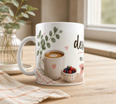 Taza de cerámica blanca con la frase "El desayuno es mi momento más especial" en tipografía marrón y rosa, con pequeños corazones y detalles de acuarela, sobre una mesa de madera con un croissant y miel de fondo.